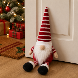 ChatGPT Image Jul 10 2026 08_13_58 AM - Butterflygifts Ltd A red-and-white striped gnome plush sits at the base of a door, with a Christmas tree and wrapped gifts visible in the background.