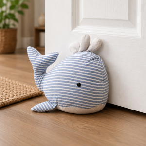 Blue striped plush whale stuffed toy leaning against a white door in a cozy room, near a woven rug.