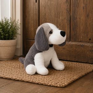 Soft plush beagle stuffed animal with gray ears and white body sits on a woven rug by a wooden door.