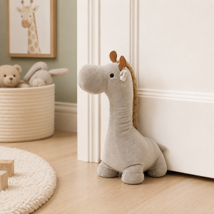 Soft gray stuffed giraffe toy standing upright by a white door in a cozy nursery, with a basket of plush animals in the background.