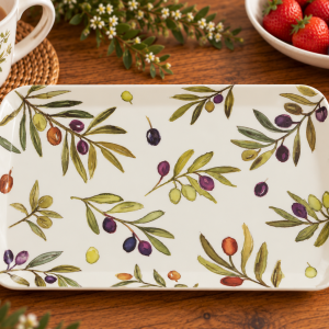 White ceramic platter with an olive branch pattern on a wooden table, surrounded by a mug, berries, and flowers for a cozy breakfast setting