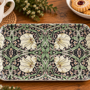 Decorative rectangular ceramic plate with an intricate cream and green floral pattern on a black background on a wooden table.