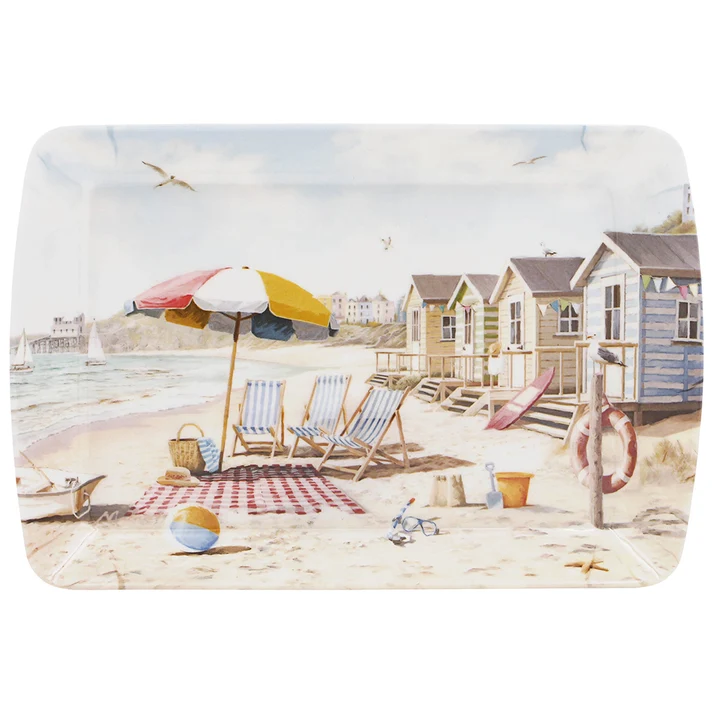 smal-tray-sandy-bay - Butterflygifts Ltd Beach scene with colorful striped chairs under a large umbrella on the sand, near beach huts and a lifebuoy by a post in the background.