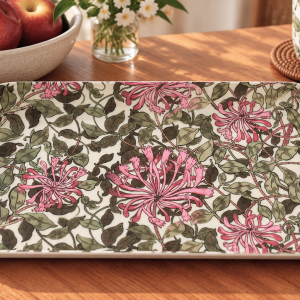 Decorative rectangular ceramic tray with pink blossoms and green leaves on white, resting on a wooden table.