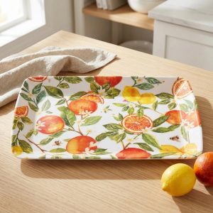 Decorative ceramic rectangular tray with orange and lemon citrus pattern on a wooden table, with a beige cloth nearby.