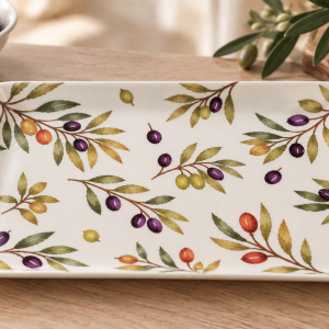 Decorative white ceramic serving plate with a colorful olive branch pattern on a wooden table.