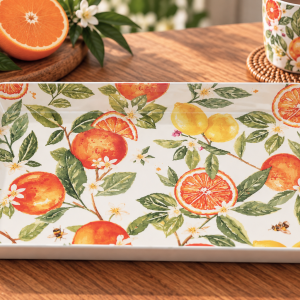 Rectangular decorative tray with orange and lemon citrus pattern on a wooden table, accompanied by a matching mug and cookies nearby.