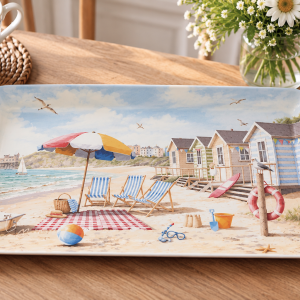 Beach-themed decorative plate showing striped chairs, umbrella, sand, and pastel beach huts by the sea.
